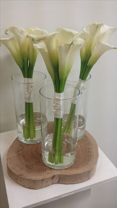 three clear vases with white flowers in them on a wooden board and some water