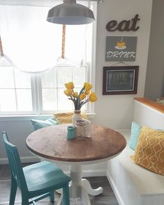 a kitchen table with two blue chairs and yellow flowers in a vase on the table