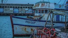 an old rusty boat sits in the water near some other boats and docks at dusk