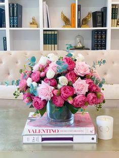 a vase filled with pink and white flowers sitting on top of a book next to a candle