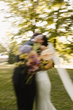 a bride and groom kissing in front of trees with their bouquets being blown by the wind