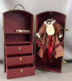 an open suitcase with clothes in it sitting on a table next to a doll's wardrobe