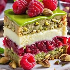 a piece of cake with raspberries and pistachios on top sits on a plate