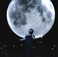 a man standing in front of the moon with his hands out and looking up at it