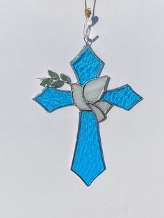 a stained glass cross ornament hanging from a rope on a white surface with blue and green accents