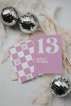 some disco balls and a pink card on a white table cloth with the number thirteen