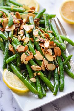 a white plate topped with green beans and almonds next to sliced lemon wedges