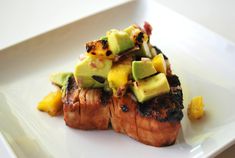 a white plate topped with meat covered in fruit and avocado on top of it