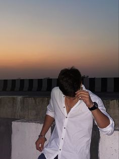 a man leaning against a wall with his hand on his face as the sun sets