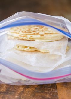 two flat breads in a plastic bag on top of a wooden table with blue and pink handles