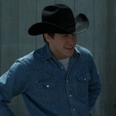 a young man wearing a cowboy hat standing in front of a wooden fence with his hands on his hips