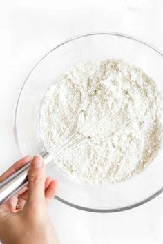 a person whisking flour into a glass bowl