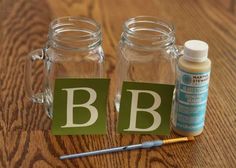 two glass jars with letters on them sitting on a wooden table next to a paintbrush