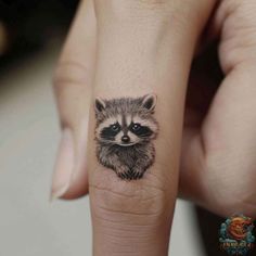 a small raccoon tattoo on the finger