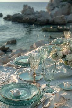 the table is set with white flowers and glassware for an elegant dinner by the ocean