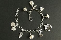 A collection of silver plated flower charms, combined with a trio of handmade flower charms designed from glass pearls in your choice of color and silver plated petals, have been dispersed around a shimmering silver plated bracelet chain in this handmade charm bracelet. This flower charm bracelet is then completed with a lobster clasp and a 1/2 inch of chain at the end for adjustable sizing. Please see the last picture in this listing for a sample view of all pearl colors available for this brac Silver Jewelry With Flower Charm, Elegant Handmade Flower Charm Bracelet, Charming Silver Jewelry With Flower Charm, Silver Metal Charm Bracelet With Pearl Charm, Elegant Flower Charm Bracelet For Jewelry Making, Silver Sterling Charm Bracelet With Flower Charm, Flower Shaped Charm Bracelet For Gift, Metal Bracelets With Flower Charm, Metal Bracelet With Flower Charm