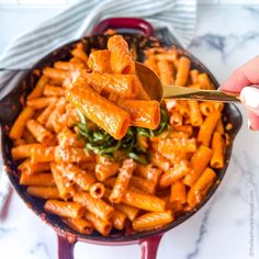 a person holding a spoon full of pasta with sauce and spinach on it in a skillet