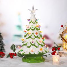 a white christmas tree sitting next to a lit candle and other holiday decorations on a table