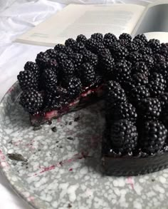 a cake with blackberries on it sitting on a plate next to an open book