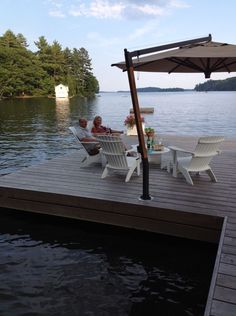 two people sitting on chairs under an umbrella at the end of a dock