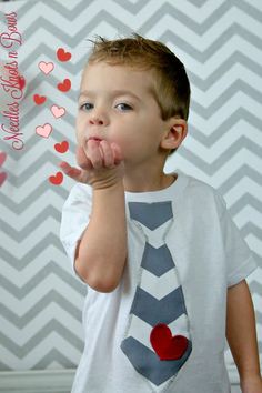 a young boy is wearing a tie and making a hand gesture with his fingers while standing in front of a chevron background