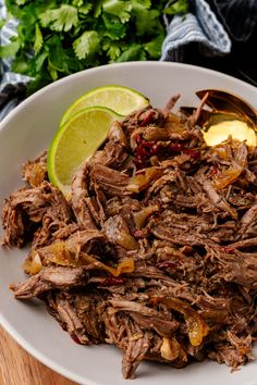 a white plate topped with sliced meat and garnish next to a lime wedge