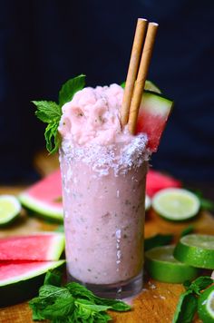 a drink with watermelon and mint garnish on the side, surrounded by sliced cucumbers