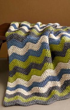 a crocheted blanket sitting on top of a wooden bench next to a wall