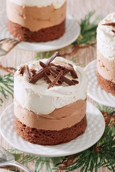 three cakes with frosting and chocolate on white plates next to evergreen branches, one has a fork in it