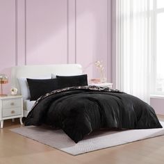 a bed with black comforter and pillows in a room next to a white headboard