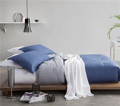 a bed with blue and white sheets in a bedroom next to a plant on the floor