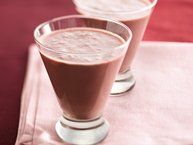 two glasses filled with chocolate drink sitting on top of a pink table cloth next to each other