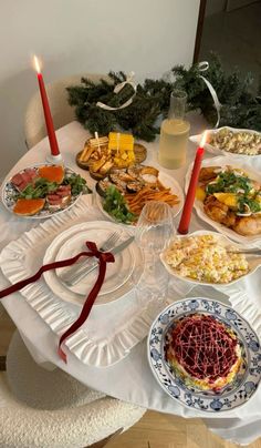 a table topped with plates and bowls filled with food next to two lit candles on top of each plate