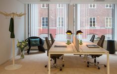 an office with two desks and chairs in front of large windows that look out onto the street