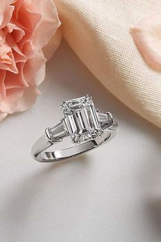 a diamond engagement ring sitting on top of a white table next to a pink flower