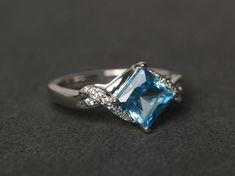 Welcome to my shop, you can find many beautiful gemstone jewelry here, and you also can ask for customized service. Main Stone: Swiss blue topaz, square cut 7X7mm,  about 2.30 carats Accent Stones: cz Metal: 925 sterling silver plated with rhodium. I also can provide metal options such as 14k solid yellow/white/rose goldSetting: prong setting More rings: https://www.etsy.com/shop/XCjewelryStudio?ref=hdr_shop_menuIt's a perfect gift for the person who was born in November (Birthstone), it's quite Blue Topaz Ring Silver, Engagement Ring Princess Cut, Engagement Ring Princess, Born In November, Ring Princess Cut, Blue Gemstone Ring, Swiss Blue Topaz Ring, Engagement Rings Princess, September Birthstone Rings