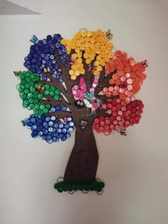 a tree made out of bottle caps on a white wall with the colors of the rainbow