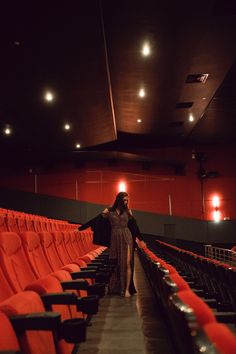 a woman standing in the middle of an empty auditorium with red seats and lights on