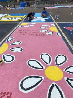 two people are sitting on the ground next to a flower painted walkway with words written on it