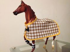 a toy horse with a blanket on it's back is standing in front of a white wall