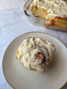 a cinnamon roll on a plate next to a casserole dish with icing