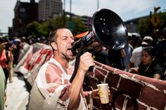 a man holding a megaphone up to his mouth while standing in front of a crowd