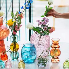 a table topped with vases filled with different colored flowers next to a hand reaching for one