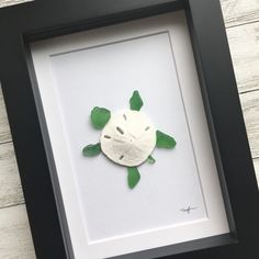 a sea turtle made out of clay in a black frame on a white wooden background