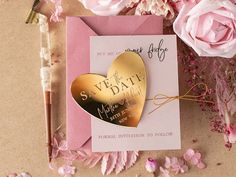 a pink and gold wedding save the date card next to some flowers on a table