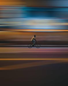 a blurry photo of a man riding a bike on the street with buildings in the background