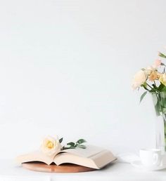 an open book sitting on top of a table next to a vase filled with flowers