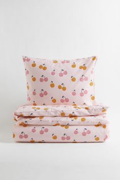 a pink bed with cherry print on the sheets and pillow cases, both made from cotton