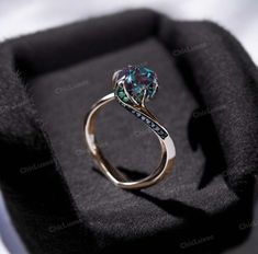 an engagement ring with blue and green stones on it in a black velvet box,