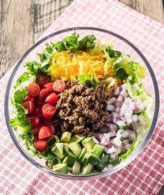 a salad with lettuce, tomatoes, meat and other ingredients in a glass bowl